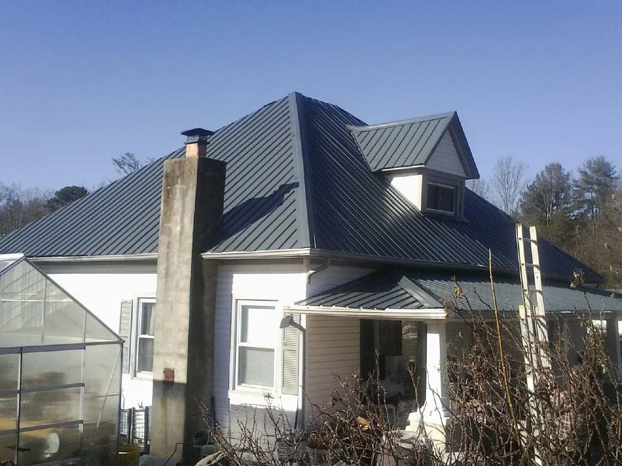 Dark blue standing seam metal roof on a white farmhouse with dormer — Slate & Tile Roof Repair by Roofing Brothers in Riga
