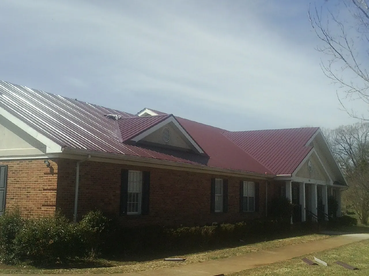 Red metal roof with gabled entries on a long brick building, from a Hail Damage Roof Repair job in Riga