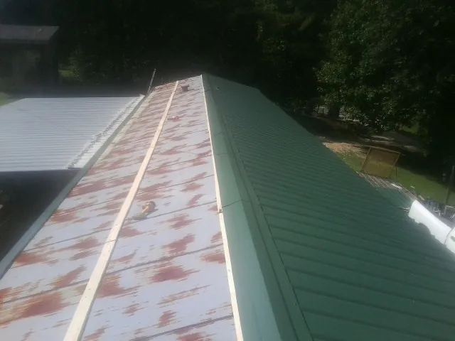 Old rusted panels beside newly installed green metal roofing — Wind Damage Roof Repair by Roofing Brothers in Riga