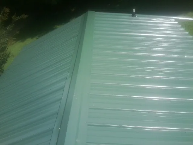 New green metal panels meeting at the ridge of a roof — Flat Roof Repair work by our crew in Riga