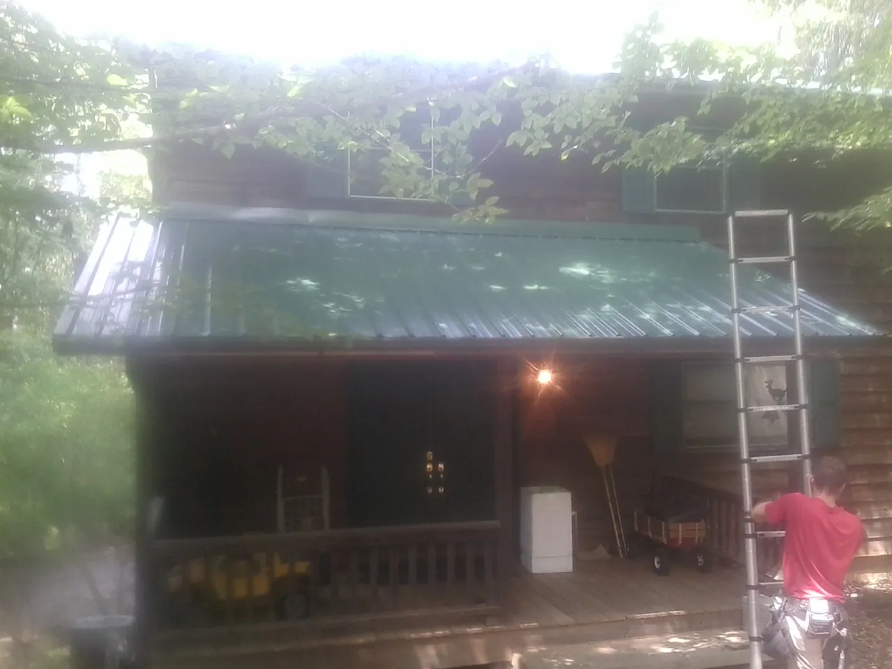Worker on a ladder at the green porch roof of a wooded cabin in Riga