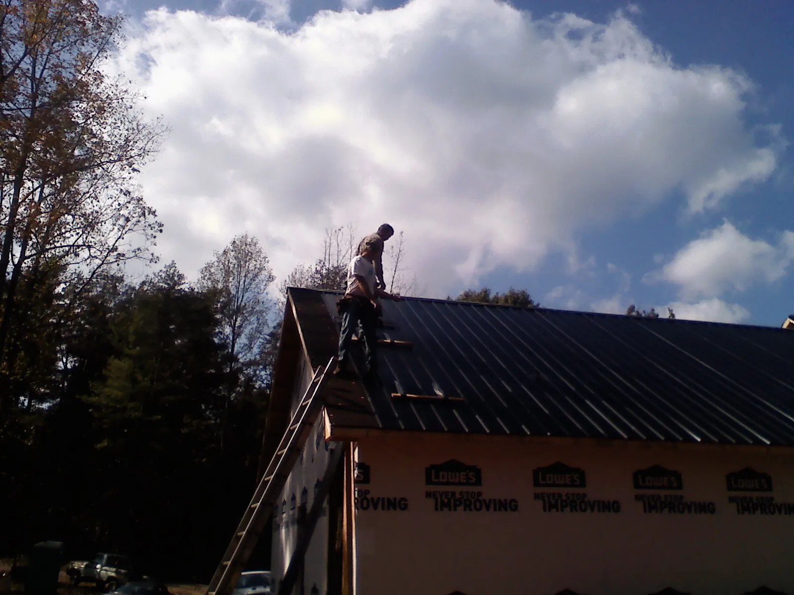 Roofer fastening dark metal panels high against a cloudy sky, from a Roof Inspection job in Riga
